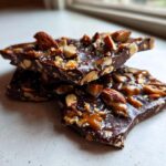 Close-up of broken pieces of dark chocolate almond toffee recipe, glistening with caramel.