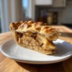 A perfect slice of homemade apple pie showing thick, caramelized apple filling and a flaky, golden-brown top crust.