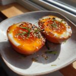 Two halves of a soft-boiled marinated eggs with bright orange yolks, topped with sesame seeds and chives.