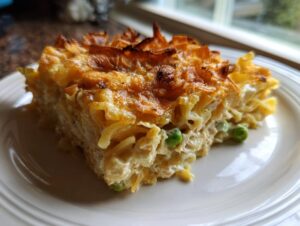 A hearty slice of baked tuna noodle casserole with a golden, crispy top and visible green peas.
