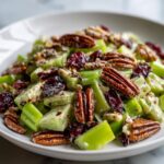 Close-up of a creamy celery salad featuring bright green chopped celery, whole pecans, and dried cranberries.