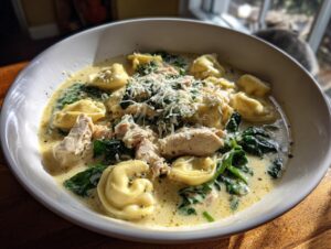 A close-up of a bowl of creamy chicken tortellini soup, filled with tortellini, shredded chicken, spinach, and topped with Parmesan.