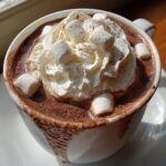 Close-up of a mug filled with rich crockpot hot chocolate, topped with whipped cream and mini marshmallows.