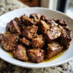 Close-up of tender crockpot steak bites coated in a savory, glistening sauce with visible spices.