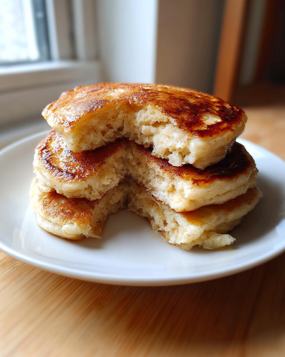 A stack of three fluffy oatmeal pancakes with a bite taken out, showing the soft interior.