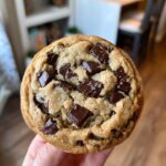 Close-up of a perfectly baked, gooey chocolate chip cookie loaded with melted chocolate chunks, held by a hand.