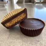 Close-up of homemade peanut butter cups, one whole and one cut in half showing the thick peanut butter filling.