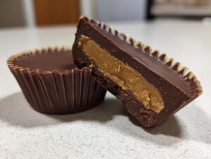 Close-up of homemade peanut butter cups, one whole and one cut in half showing thick chocolate and creamy filling.
