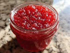 Close-up of a glass jar filled with bright red, textured strawberry freezer jam.