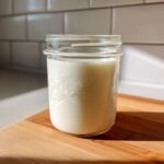 A jar filled with creamy homemade coffee creamer sitting on a wooden cutting board.