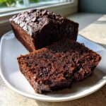 A slice cut from a loaf of rich, dark chocolate zucchini bread topped with chips.