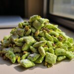 A close-up pile of bright green pistachio puppy chow coated in powdered sugar and mixed with whole pistachios.