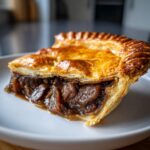 Close-up of a slice of savory meat pie showing rich, dark filling and flaky golden crust.