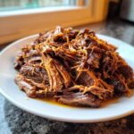 A close-up of tender, shredded Mississippi pot roast piled high on a white plate, glistening with juices.