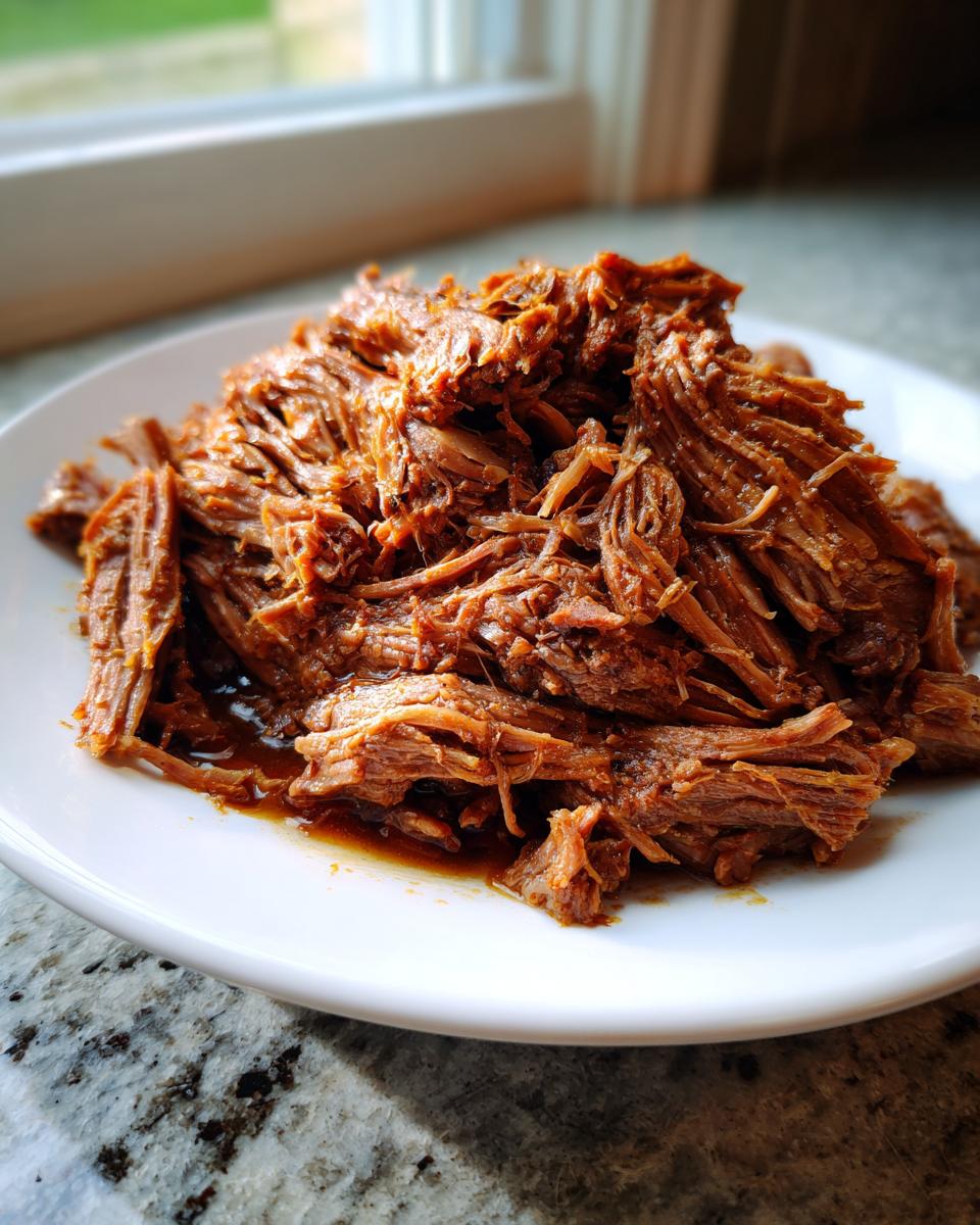Close-up of tender, shredded mississippi pot roast piled high on a white plate with natural light.