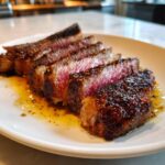 Five perfectly sliced pieces of medium-rare ribeye steak showing a deep pink center and dark sear, resting in pan juices.