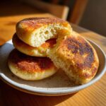 Close-up of three golden-brown sourdough english muffins, one split open revealing many nooks and crannies.
