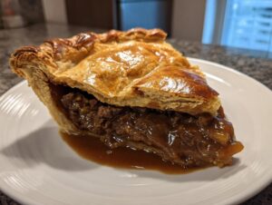A close-up of a slice of savory meat pie showing a rich, dark filling and a golden, flaky top crust.