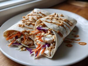Two delicious thai peanut chicken wraps filled with chicken and slaw, drizzled with peanut sauce and topped with crushed peanuts.