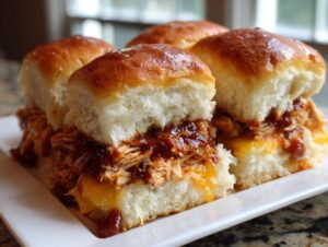 Four glistening bbq chicken sliders filled with pulled chicken, melted cheddar cheese, and rich BBQ sauce, served on a white platter.