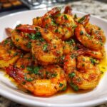 Close-up of juicy, orange Cajun shrimp coated in spices and fresh parsley, sitting in a buttery sauce.