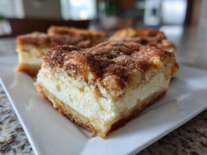 A close-up of a thick slice of churro cheesecake bars showing the creamy filling and cinnamon-sugar topping.