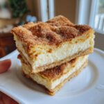 Two stacked portions of creamy churro cheesecake bars topped generously with cinnamon sugar.