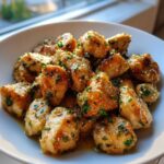 Close-up of golden brown garlic butter chicken bites coated in sauce and fresh parsley, served in a white bowl.