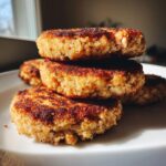 A stack of three golden-brown, pan-seared salmon cakes piled on a white plate.