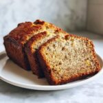 Close-up of a loaf of moist sugar free banana bread, sliced and served on a white plate.